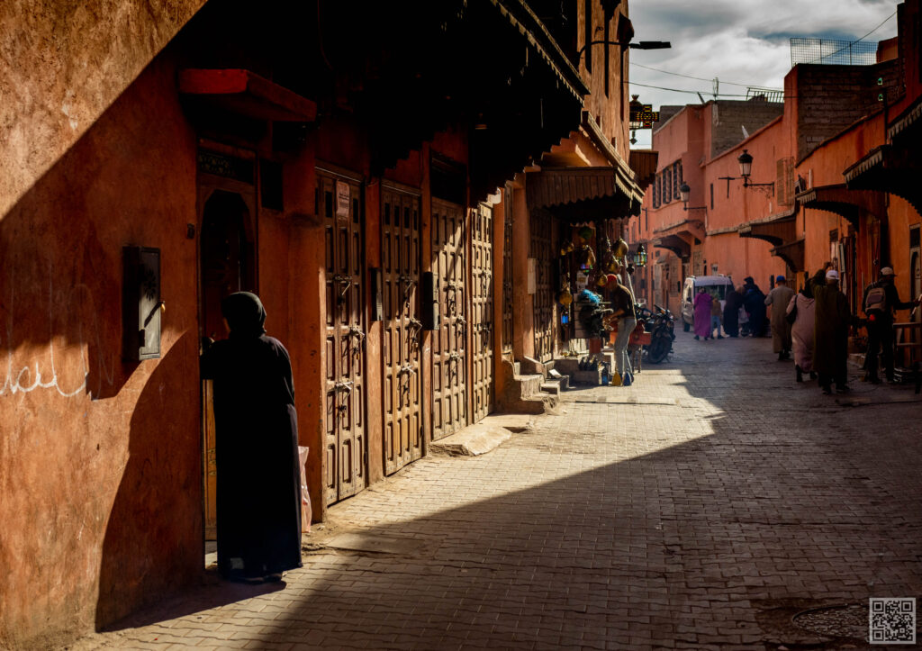 Busy street scene in Marrakesh Medina early in the morning with colorful buildings and few people visible.