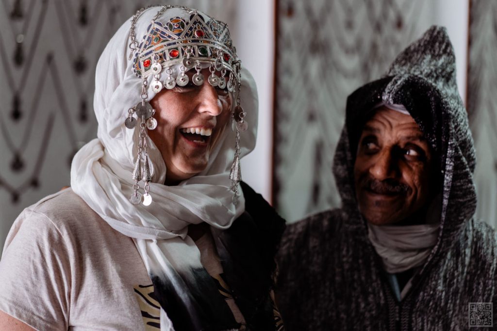A tourist tries on a traditional headpiece with a smile at a Moroccan artisan shop.